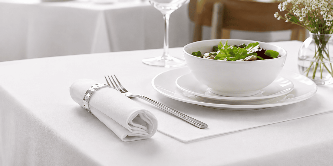 Mesa de restaurante vestida con mantel blanco de satén y servilletas dobladas