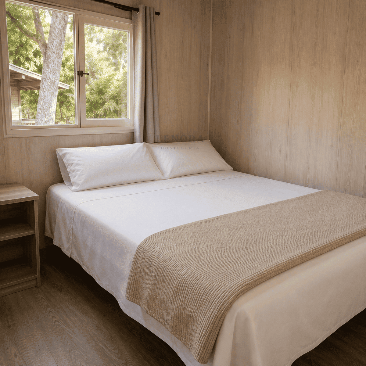 Interior de un bungalow de camping con cama vestida con ropa de cama blanca