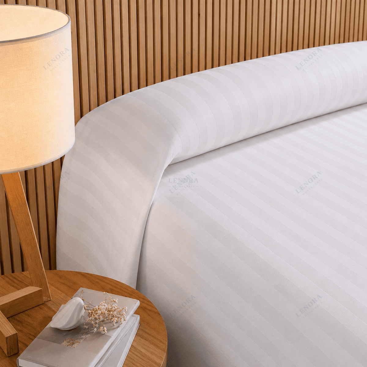 Cama de hotel vestida con colcha de cutí blanca junto a una lámpara