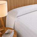 Cama de hotel vestida con colcha de cutí blanca junto a una lámpara