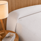 Cama de hotel vestida con colcha Otomán blanca junto a una lámpara