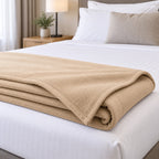 Manta ignífuga beige plegada al pie de una cama de hotel