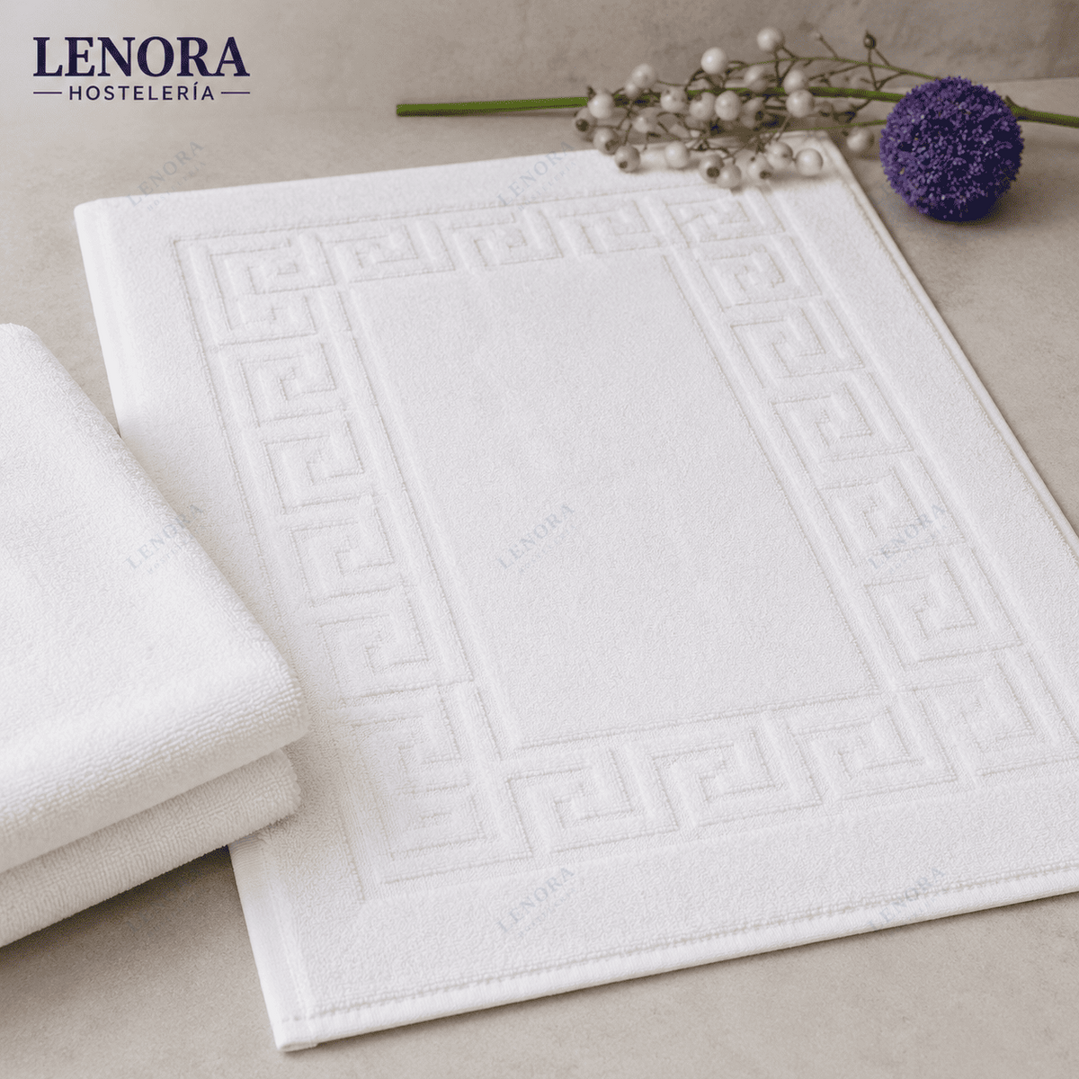 Alfombrín de baño blanco con cenefa de greca junto a flores secas